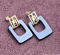 Top down photo of the pair of 10K gold earrings with grey rectangular hollow pendants on a purple fabric.