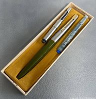 Green Parker fountain pen with silver cap and two silver pen accessories in original box, showing box interior and contents.