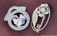 Photo showing circular Girl Guides of Canada brooch with enamel and silver floral brooch.