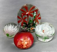 Four vintage glass paperweights with floral and Pharaoh designs arranged on neutral background
