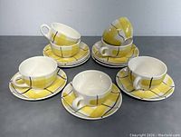 Seven cups stacked or arranged on matching saucers with yellow Calico pattern and black lines on a white base.