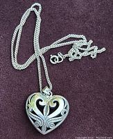 Silver twisted rope chain with heart pendant laid flat on purple fabric background