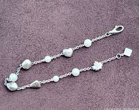Top view of the Birks sterling silver bracelet laid out to display chain, silver hearts, silver beads and white beads.
