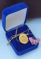 Blue velvet box containing a gold tone necklace with a round pendant and a pink rhinestone butterfly pin.