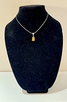Front view of the necklace displayed on a black bust showing the amber pendant and chain length.