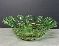 Front side view of green glass basket bowl showing ruffled rim and hand painted flower details.