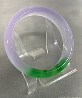 Multi-color jade bangle on a clear plastic stand showing purple and green hues