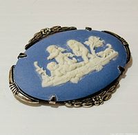 Close up photo of the front of the oval brooch showing blue jasperware cameo with white cherub relief and silver floral border.