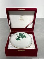Porcelain bowl with green floral decoration and gold rim inside white padded lining of red velvet box. Lid interior marked 'PISA 1877'.
