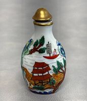 Front side view of the porcelain snuff bottle showing pagoda, trees, and a boat with a figure wearing red.