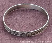 Front side view of vintage sterling silver bangle on purple background showing floral engraved design