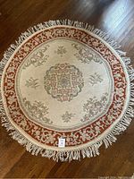 Top-down view of entire round area rug showing central medallion and rust-colored border with fringed edges.