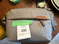 Front view of a gray Peak Design crossbody bag with a front zipper pocket and brown leather brand tag.