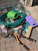 Photo of assorted garden tools including watering can, pruning shears, hammer, wire basket, wire brush, and coiled garden hose.