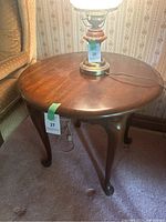 Full view of the round cherry wood side table with a lamp placed on top, showing the wood grain and surface condition.