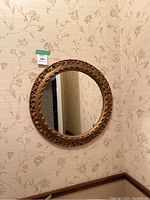 Full view of round mirror mounted on floral wallpapered wall, showing gold rim with textured design.