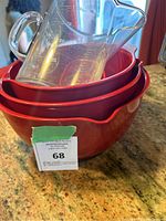 Three nested red plastic mixing bowls with spouts and clear glass measuring cup on top on countertop.