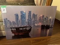 Photo of the metal art featuring a city skyline and traditional boats on the water at night.