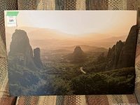 Photorealistic wall art panel showing mountains and large rock formations with valley and greenery in warm light, measuring approximately 30x20 inches.