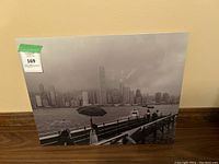 Front view of black and white metal art depicting city skyline in rain with umbrella holders in foreground.