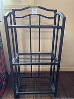 Front view of black metal 3-shelf stand showing three open slatted shelves and curved top rail