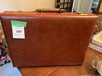 Front side of brown leather briefcase with a sticker tagged with "147" placed on the surface.