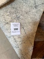 Close-up of the padding layer underneath the rug, showing thick texture and auction tag with lot number 180.
