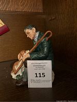 Side view of Royal Doulton figurine showing man holding cane and petting dog, with auction label visible