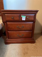 Front view of the solid wood bedside table showing three drawers with brass handles and knobs.