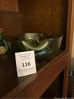 Large green glass chip bowl with scalloped edges shown on a wooden shelf with auction tag.