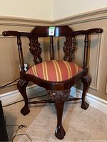 Front view of the vintage oriental mahogany corner chair showing carved claw feet, decorative backrest and upholstered striped seat.