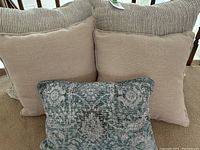Set of three accent pillows showing two beige textured pillows and one smaller patterned pillow in green and gray tones.