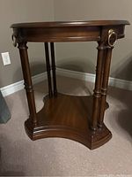 Front side angle of the wooden accent table showing the turned legs and brass ring pull detail.