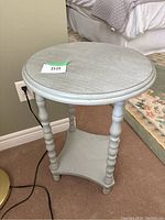Full view of rustic gray two-tiered round accent table beside a bed, showing top and legs.