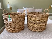 Pair of round rattan baskets with looped handles, placement on a bed showing their size and shape.