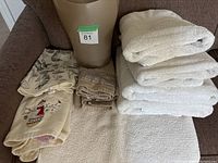 Full set of towels folded and stacked on a chair along with a tall beige garbage bin.
