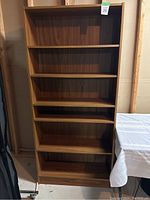 Full view of the tall wooden bookcase with five adjustable shelves in a medium brown finish, showing overall good condition.