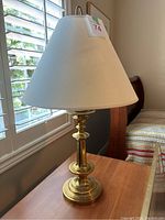 Brass table lamp on a wooden surface near a window, showing overall condition and style.