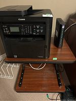 Full view of the Canon ImageCLASS MF4550d printer on wooden stand with modem/router.