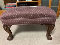 Side profile view of the footstool showing upholstered seat and carved wooden legs with lion paw feet.