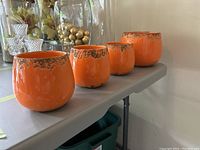 Four orange ceramic garden pots with decorative texture on rim, placed on a table.