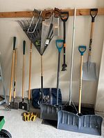 Wide view of all the garden tools together against the wall showing shovels, rakes, saws, and accessories