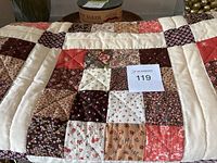 Close-up of quilt patchwork showing fabric squares in various floral and polka dot patterns in red, brown, beige and cream.