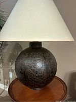 Photo of the lamp base showing dark brown cracked leather-look spherical design on wood surface.
