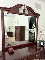 Front view of large dresser mirror with reddish-brown wooden frame and decorative finial top.