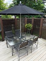 Full view of the outdoor dining set including table, four chairs, black umbrella and fencing background.