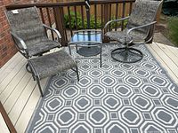 View of two swivel chairs, one ottoman, side table, and area rug arranged outdoors on a deck with wooden railings.