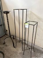 Three iron pieces including two glass-topped plant stands and one twisted stem candleholder shown from overview angle.