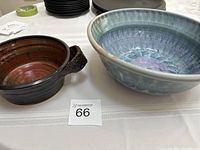 Two pottery bowls on a table, one dark brown with reddish tones and handles, the other a larger blue glazed bowl.