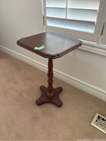 Side view of the fold down top table showing the pedestal leg and four-legged base on carpeted floor.